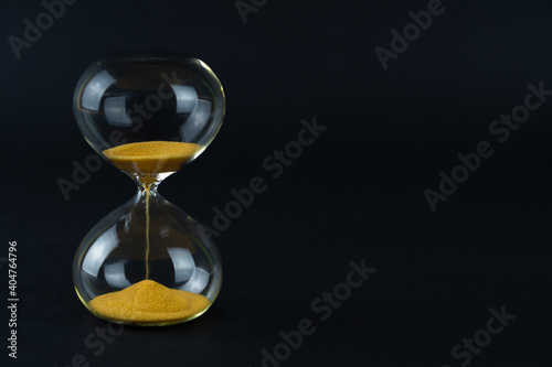 Hourglass with golden sand and black background, copy space