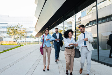Group of business people walking outside in front of office buildings.