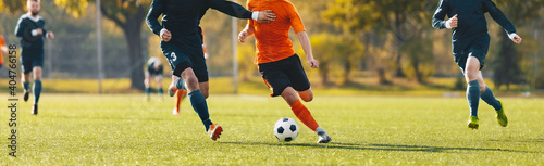 Horizontal image of football players running in a duel on a tournament match. Soccer forward player compete with defender. Anonymous football players kicking league game