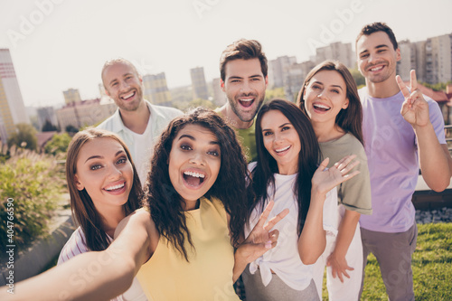 Photo portrait of students company taking selfie waving showing v-sign gesture smiling outdoors in summer with city view
