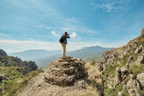 a tourist stands on a rocky hillock and takes pictures of the mountains
