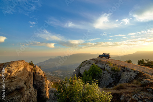 Jeep near a steep cliff against the background of mountains and the setting sun in the blue sky