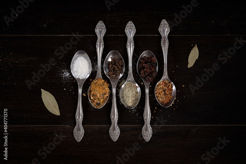 different spices and spices on a spoon on a dark wood background (ID: 404771370)