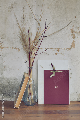 still life in the form of a glass transparent vase with dried grass and books on the background of a vintage wall (ID: 404771391)