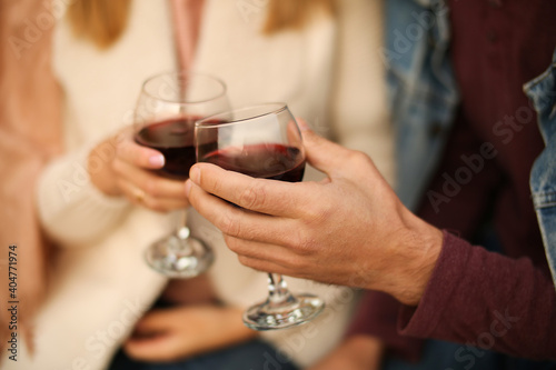 Two glasses of red wine close-up in hands outside the house. Man and woman in love make the clink of glasses. Celebrate Valentine s Day  date. Warm  blurred background  countryside relaxation.