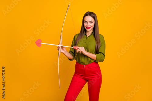 Portrait of gorgeous slim cheerful straight-haired girl shooting heart arrows isolated over bright yellow color background