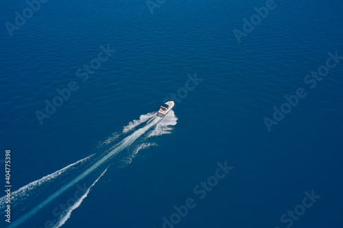 Aerial view of a boat with an awning in motion on blue water. Top view of a white boat sailing in the blue sea. luxury motor boat. Drone view of a boat sailing at high speed. © Berg