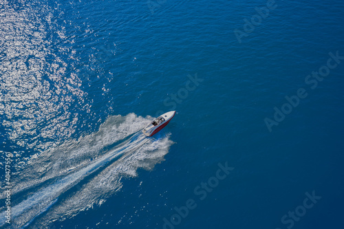 Aerial view of a boat in motion on blue water. Boat in the sun. Top view of a white boat sailing in the blue sea. luxury motor boat. Drone view of a boat sailing at high speed.