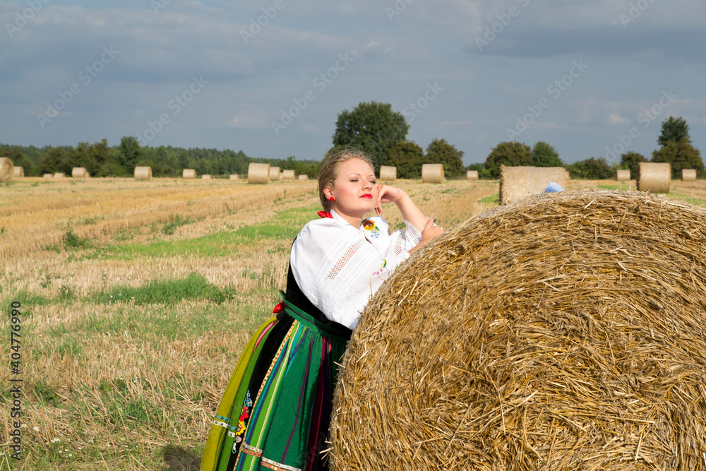 A portrait of a pretty young smiling blonde woman dressed in Polish national folk dress in the field of harvest straw bales A portrait of a pretty young smiling blonde woman dressed in Polish national folk dress in the field of harvest straw bales