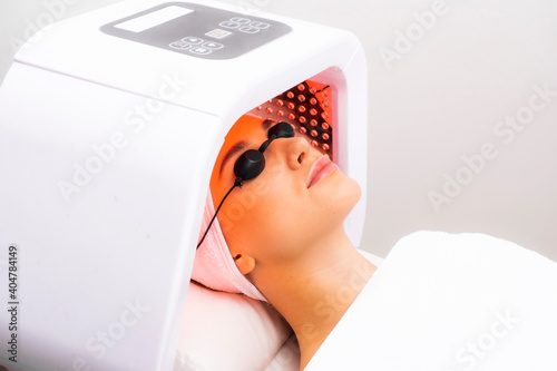 Express facial treatment with led therapy. Beautiful girl on a light therapy procedure. LED lamp with red light.