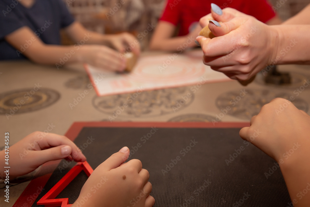 Obraz premium Cooking at home: mother with children makes cookies, gingerbread. On a table covered with a tablecloth, dough, rolling pin, cookie molds, the hands of children and women at work.