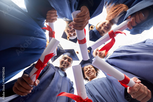 education, graduation and people concept - group of happy international graduate students in mortar boards and bachelor gowns with diplomas