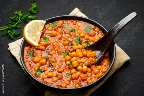 Chana Masala or Chole in black bowl on dark slate table top. Indian cuisine veg chickpeas curry dish. Asian spicy vegetarian food and meal. Close up