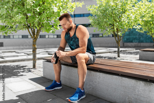 fitness, sport and people concept - tired young man with bottle of water sitting on city bench