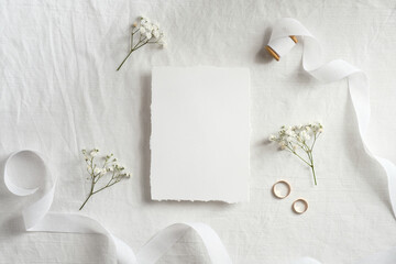 Wedding invitation card template. Top view blank paper card, ribbon, golden rings, flowers on white background.