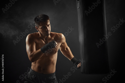 male boxer in black boxing wraps punching in boxing bag on dark background with smoke © producer