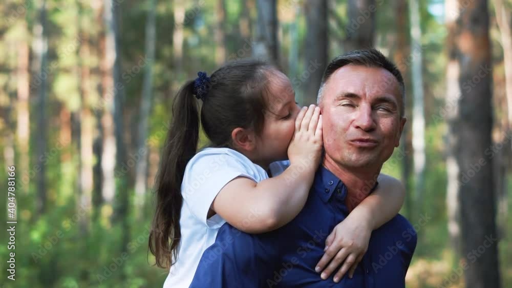 The daughter sits on her dad's back and whispers in his ear The daughter sits on her dad's back and whispers in his ear