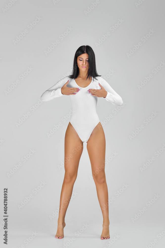 beautiful slim tanned woman with perfect body and long legs in white  bodysuit posing over studio background. Stock Photo