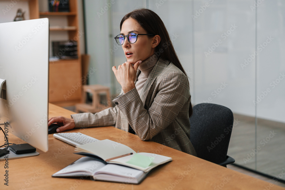 Focused charming woman in eyeglasses working with computer and planner Focused charming woman in eyeglasses working with computer and planner