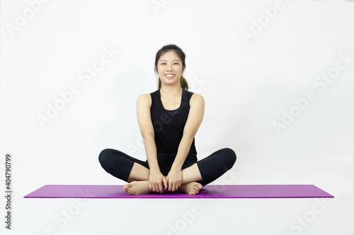 Asian woman sitting on a yoga mat, smiling pose and looking at the camera, Asian woman wearing a black shirt on a white background.