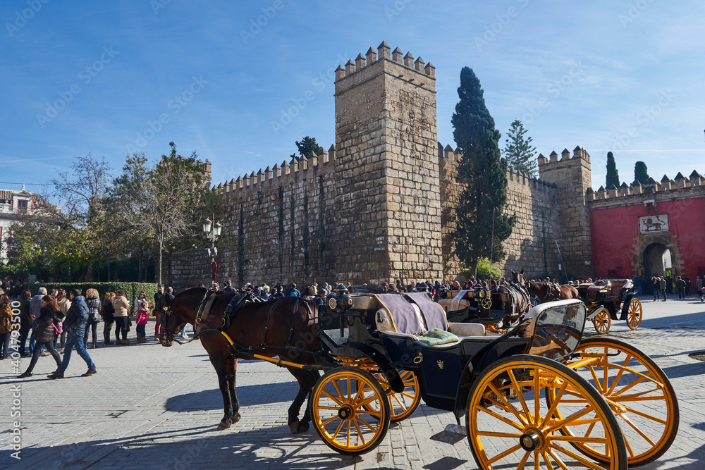 Fototapeta premium Seville, Andalusia, Spain, Europe. Horse carriage and view of the Lion's Gate in the Real Alcazar of Seville and row of people waiting to enter