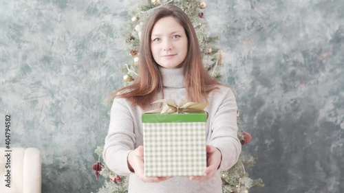 A beautiful woman stretches a bright box with a Christmas present forward to the camera. photo