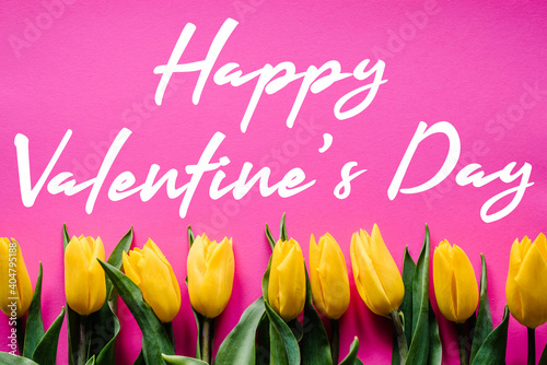Row of yellow tulips on pink background with text message. Holiday greeting card for Valentine's. Top view, flat lay.