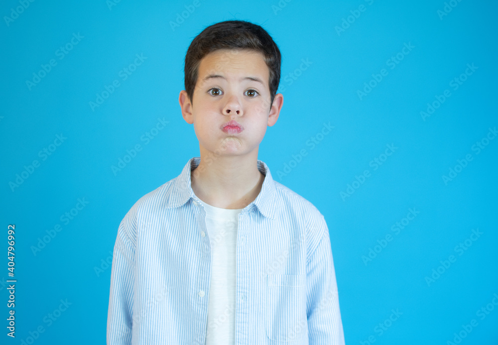 Beautiful kid boy wearing casual shirt standing over isolated blue background puffing cheeks with funny face. Mouth inflated with air, crazy expression. Beautiful kid boy wearing casual shirt standing over isolated blue background puffing cheeks with funny face. Mouth inflated with air, crazy expression.