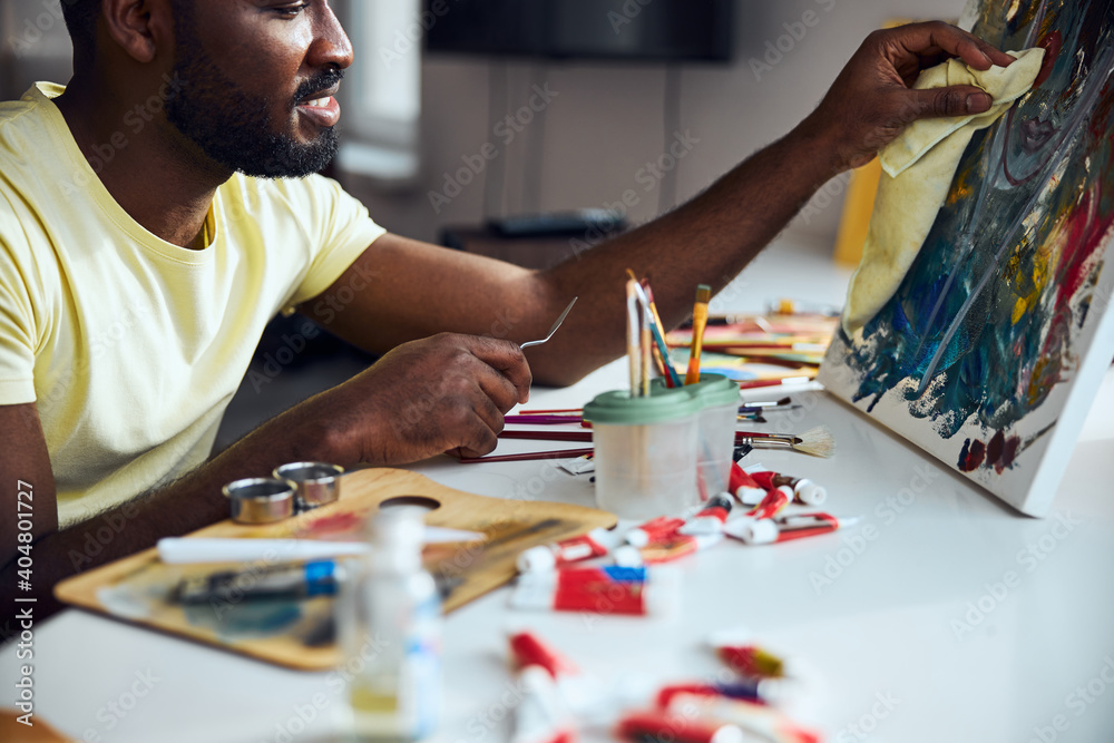 Fototapeta premium Multiracial artist touching a painting with a rag
