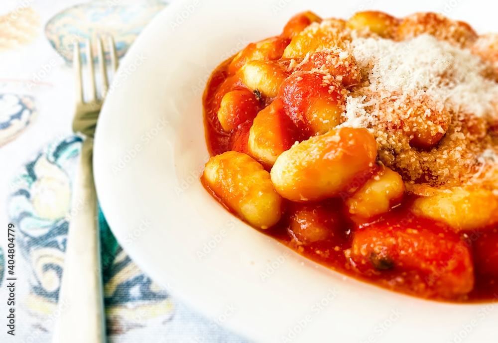 Portion of gnocchi in tomato sauce with grated parmesan cheese served in a white ceramic plate. Portion of gnocchi in tomato sauce with grated parmesan cheese served in a white ceramic plate.