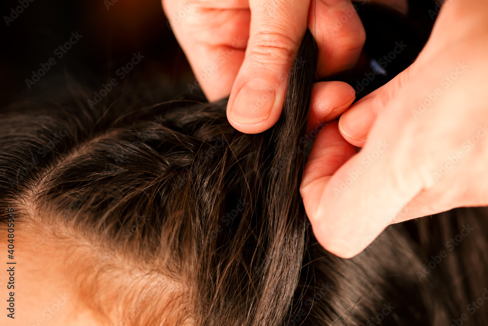Fototapeta premium Woman hands braiding brunette girls long hair.