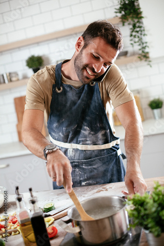Attractive man cooking in modern kitchen. Handsome man talking to the phone while cooking.