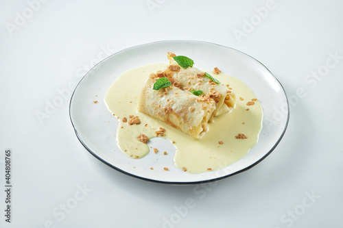 A dish of Ukrainian cuisine - pancakes stuffed with cottage cheese with sweet creamy sauce on a white plate on a white plate. Blini or french crepes