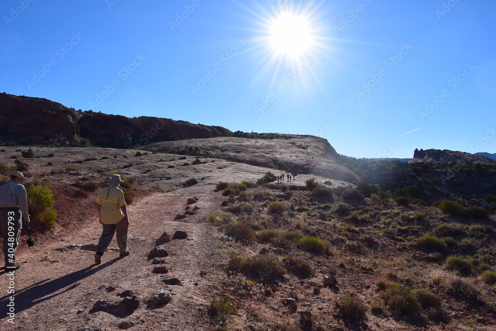 Man hiker with hat hiking on desert path towards into sun Man hiker with hat hiking on desert path towards into sun
