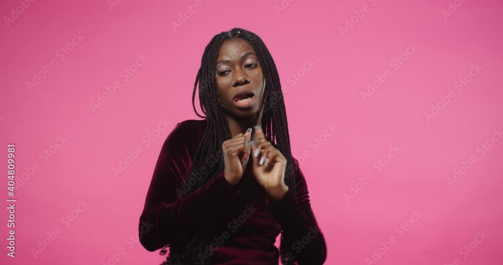 Close up portrait of joyful African American young beautiful brunette woman dancing making funny moves over pink wall background in studio smiling and looking at camera with happy face. Fun concept
