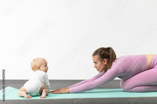 Young woman in sportswear workout together with her baby. Happy mother with son doing plank yoga exercise. Concept of active lifestyle and motherhood