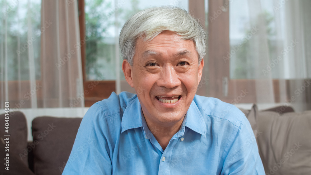 Asian senior man video call at home. Asian senior older Chinese male using mobile phone video call talking with family grandchild kids while lying on sofa in living room at home concept. Asian senior man video call at home. Asian senior older Chinese male using mobile phone video call talking with family grandchild kids while lying on sofa in living room at home concept.