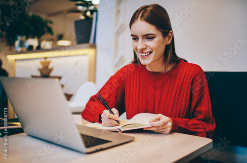 Happy young female freelancer working remotely in modern restaurant