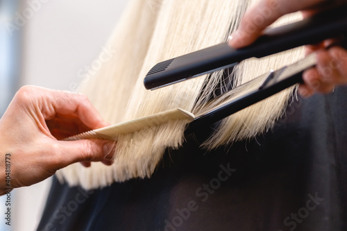 Hairdresser straightens blonde hair with flat iron