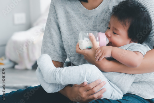 Young asian mother feeding baby from milk bottle.