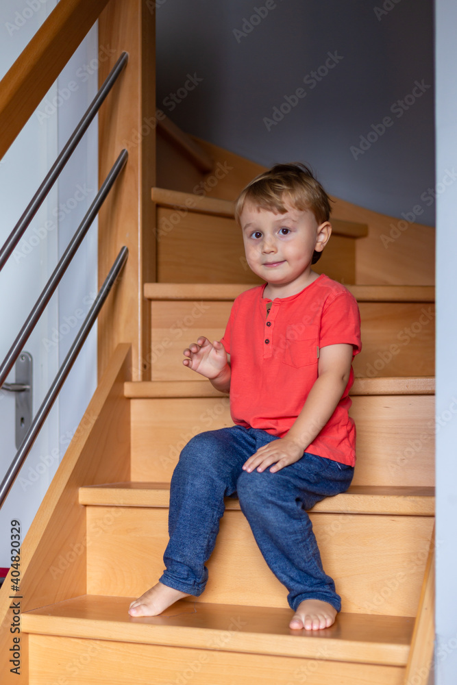 Little boy waering t-shirt is sitting on the stairs at home. Barefoot child. Safety house for children. Little boy waering t-shirt is sitting on the stairs at home. Barefoot child. Safety house for children.