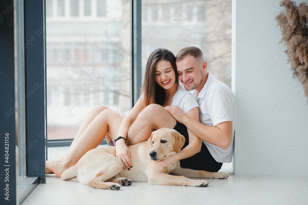 Happy Loving Family Concept. Portrait of beautiful couple with dog sitting on the floor in modern apartment Happy Loving Family Concept. Portrait of beautiful couple with dog sitting on the floor in modern apartment