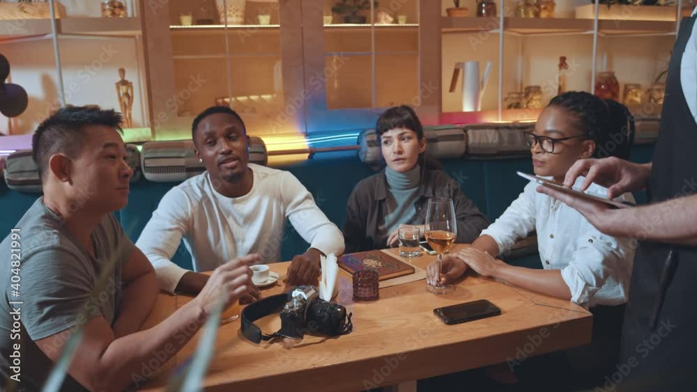 Best friends company socializing in cafeteria. Young waiter asking order making notes in digital tablet. Communication. Social gathering. Public place. Best friends company socializing in cafeteria. Young waiter asking order making notes in digital tablet. Communication. Social gathering. Public place.