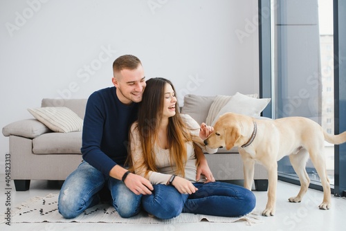 Young beautiful couple with dog sitting on the floor at new home.