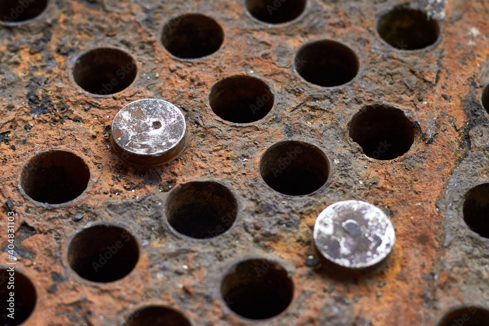 Tube sheet or plate of heat exchanger boiler closeup selective focus background disconnected muted clogged leaky tubes with steel plugs with insoluble hard mineral deposits salts scale and corrosion. Tube sheet or plate of heat exchanger boiler closeup selective focus background disconnected muted clogged leaky tubes with steel plugs with insoluble hard mineral deposits salts scale and corrosion.