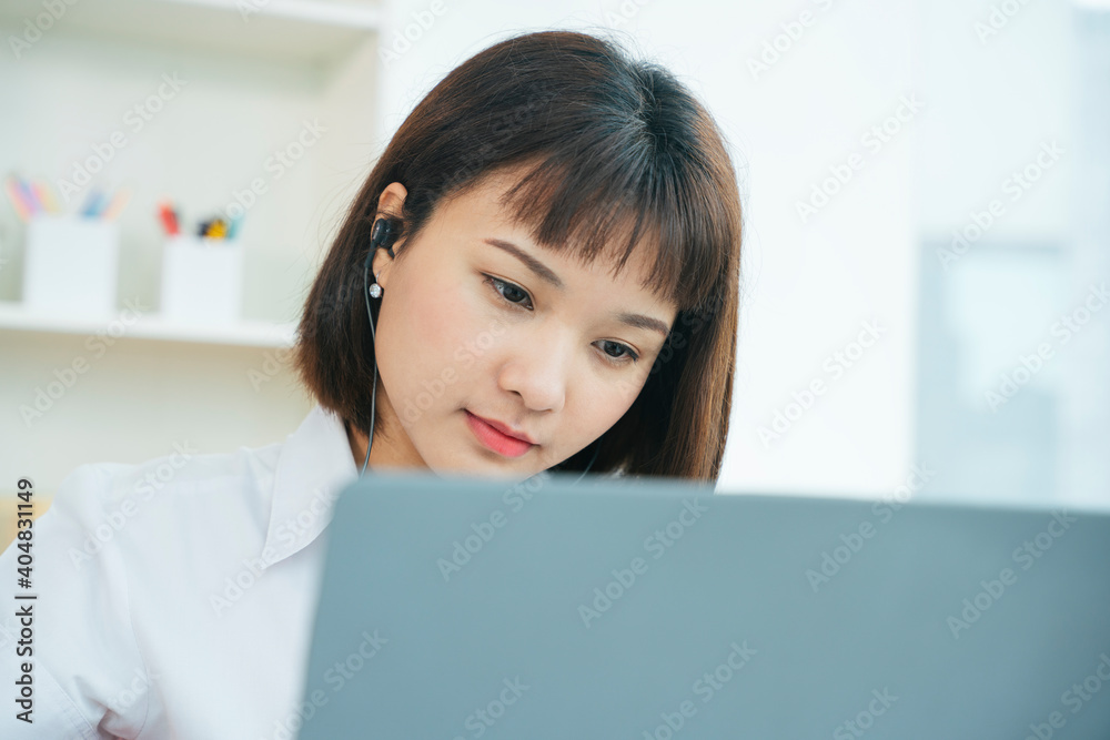 Asian thai university student study from home wearing earhpones looking at laptop. Asian thai university student study from home wearing earhpones looking at laptop.