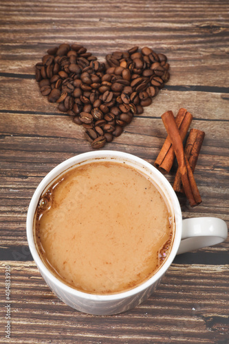 Top view of heart shaped coffee beans and white coffee mug against wooden background. Coffee lovers. 