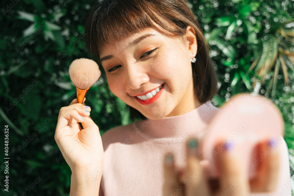 Asian thai woman apply cosmetic brush over green nature background outdoors. Asian thai woman apply cosmetic brush over green nature background outdoors.