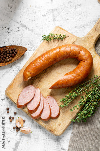 Smoked Cracow sausage on a wooden serving board on a light gray kitchen table. Slicing boiled and smoked sausage
