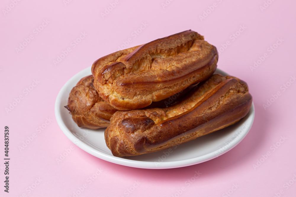 Eclairs on a pink background. Three eclairs on a white plate. Sweet breakfast. Eclairs on a pink background. Three eclairs on a white plate. Sweet breakfast.